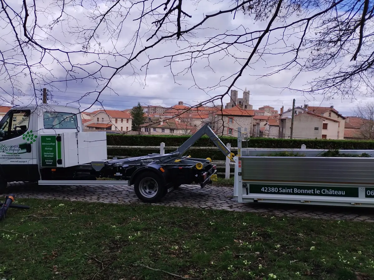 Camion MDF Paysage équipé d'un bras ampliroll et sa benne d'évacuation, devant le village de Saint-Bonnet-le-Château