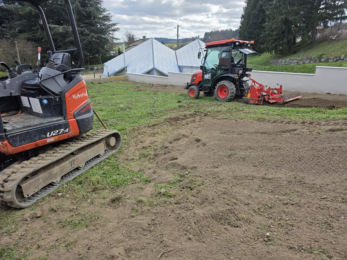 Mini-pelle et micro-tracteur équipé d'une herse rotative préparant la terre d'un terrain avant engazonnement