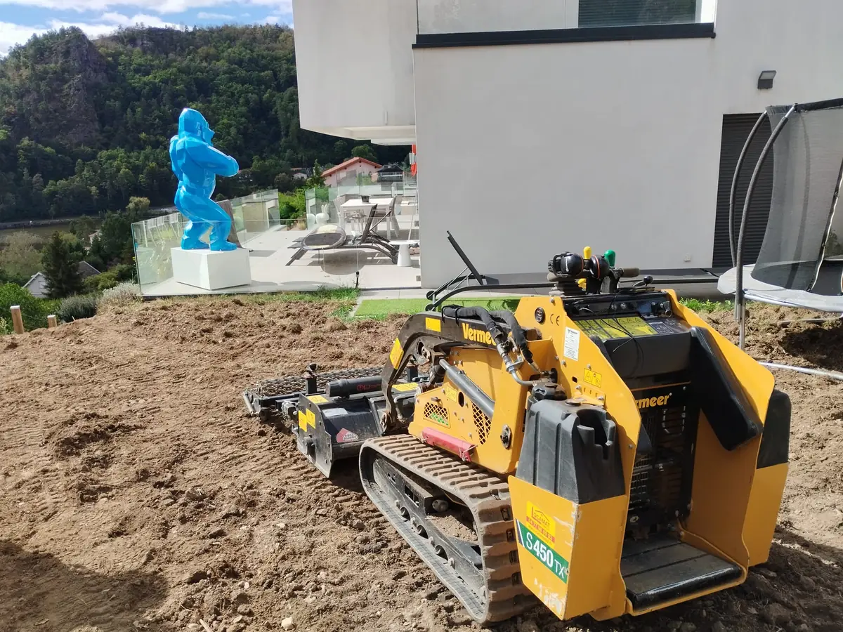 Mini-chargeuse à chenilles en terrassement sur le terrain en terre nue d'une maison contemporaine